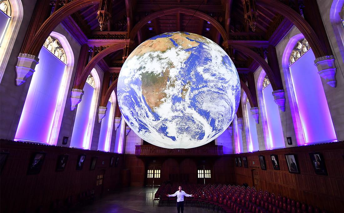 Artist Luke Jerram stands underneath a replica of the earth