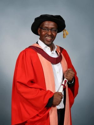 Latif Ismail smiles while wearing graduation gown and holding his diploma
