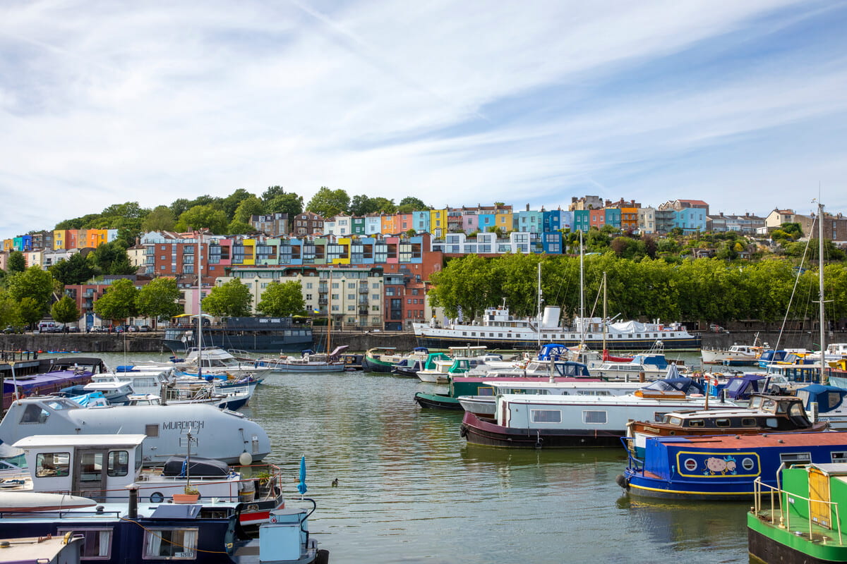 A colourful view of the Bristol Harbourside with many boats and rainbow coloured houses in the background.