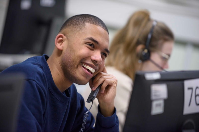A student telethon fundraiser is smiling as he holds the phone to his ear. 